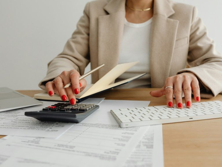 Steuerrecht Eine Person mit roten Nägeln blättert in einem Dokument auf einem Schreibtisch.